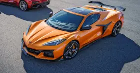 Pomarańczowy Chevrolet Corvette C8 z czarnym dachem i spojlerem na torze wyścigowym. Obok widać fragment czerwonego samochodu.