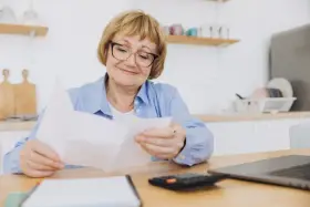 Uśmiechnięta starsza pani z okularami przegląda dokumenty, planując wymianę dowodu osobistego po 70 roku życia.