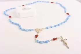 Niebieski różaniec z czerwonymi akcentami i krzyżem. Wybór różańca na roczek symbolizuje błogosławieństwo i duchową drogę.