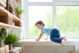 Małe dziecko raczkuje po parapecie. Warto zadbać o zabezpieczenia przed dziećmi, by uniknąć niebezpiecznych sytuacji.