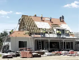 Ekipa budowlana pracuje nad remontem dachu domu. Widać rusztowania, drabiny i materiały budowlane.