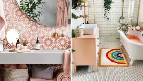 Une salle de bain bohème avec des carreaux floraux roses, un tapis arc-en-ciel et une baignoire remplie d'eau orangée.