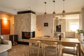 Przytulny salon z kominkiem i jadalnią w stylu klasycznym. Drewniany stół z krzesłami, kanapa i nowoczesny kominek tworzą ciepłą atmosferę.
