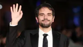 Valerio Vestoso saluta con la mano, sorridendo con un abito elegante.