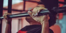 Mężczyzna wykonuje podciąganie na drążku, jego dłonie mocno zaciskają metal.