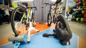 Dwa rowery na trenażerach, jeden z napędem direct drive, gotowe do treningu w sklepie sportowym.
