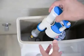 Mano instalando un nuevo mecanismo de descarga para cambiar la cisterna del inodoro.