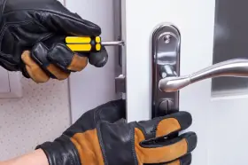 Mains gantées ajustent un loquet serrure bloqué sur une porte blanche avec un tournevis.