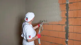 Pracownik nakłada tynk maszynowy na ścianę z cegły. Sprawdź atrakcyjną tynki maszynowe cenę!