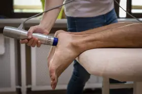 Fizjoterapeuta stosuje falę uderzeniową na stopę pacjenta, by leczyć uciążliwe ostrogi.