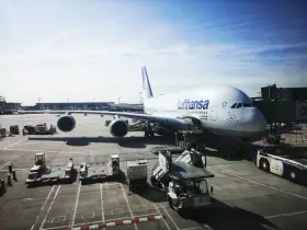 Lufthansa A380 na płycie lotniska we Frankfurcie. W tle widać inne samoloty i budynki terminali, typowe dla lotnisk w Niemczech.