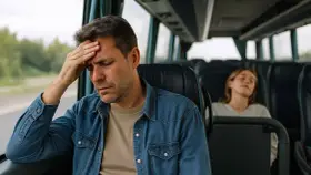 Mężczyzna z ręką na czole w autobusie, cierpiący na chorobę lokomocyjną. Obok śpi młoda kobieta.