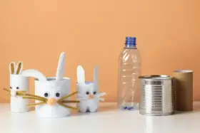 Zające z rolek po papierze i puszek to świetne przykłady recyklingu w życiu codziennym. W tle pusta butelka i rolka po ręczniku papierowym.
