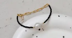 Elegancka bransoletka z czarnego onyksu i perły, z elementami złotej biżuterii. Czy onyks jest drogi? Ten wygląda na wart swojej ceny.
