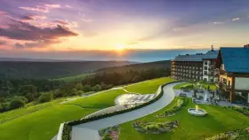 Hotel Arłamów z basenem i tarasem, otoczony zielonymi wzgórzami o zachodzie słońca. Ile pokoi ma hotel Arłamów? Tego nie widać, ale jest ich wiele!