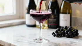 Un verre de vin rouge est servi, avec des grappes de raisin noir à côté. Le vin aligoté, souvent blanc, ici rouge, évoque la fraîcheur et la vivacité.
