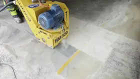 Żółta maszyna do szlifowania betonu RM-320 pracuje na posadzce, tworząc pył.