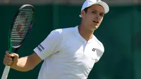 Hubert Hurkacz w białej koszulce i czapce, gotowy do uderzenia rakietą na Wimbledonie.