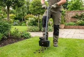 Gartenarbeit nach dem Winter: Ein Mann belüftet den Rasen mit einem speziellen Werkzeug, um ihn für die neue Saison vorzubereiten.