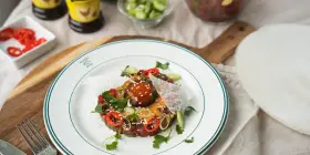 En läcker asiatisk råbiff med chili, salladslök och sesamfrön, serverad på en vit tallrik med gröna kanter.