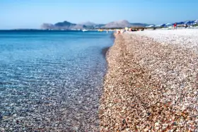 Rodos: turkusowe morze obmywa kamienistą plażę, w tle góry i plażowicze. Idealne miejsce na wakacje.