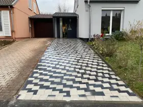 Une allée en pavé au motif géométrique noir et blanc mène à une entrée de garage.