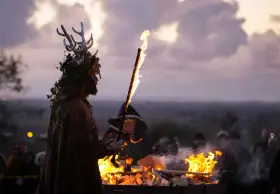 En person med hjorthorn och lövverk håller en fackla vid en eld. En mystisk stämning under halloween i Irland.