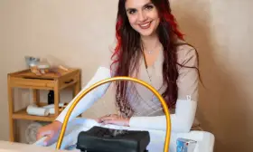 Uśmiechnięta stylistka z rudymi pasemkami przygotowuje się do zabiegu. Dowiedz się, ile kosztuje pedicure w tym salonie.