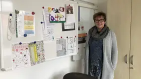 Lehrerin mit Lernmaterialien, darunter ein Kreuzworträtsel mit Gegenteilen und eine Liste von Verben, die das present participle zeigen.