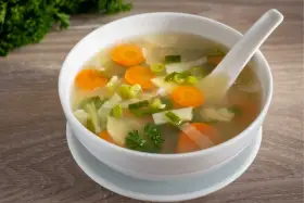 Tazón de sopa de verduras con zanahorias, puerros y perejil.