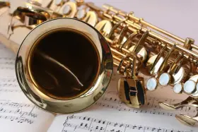 Ein glänzendes Musikinstrument, ein Saxophon, liegt auf Notenblättern. Seine goldene Oberfläche reflektiert das Licht.