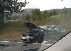 Zniszczony samochód po wypadku, maska otwarta, widoczne uszkodzenia. DKL rejestracja widoczna na przodzie pojazdu.