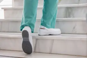 Persona subiendo escaleras con zapatos blancos, mostrando la suela antideslizante. El poliuretano en zapatos ofrece comodidad y durabilidad.