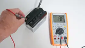 Una mano usa il multimetro per misurare la tensione di una batteria, mostrando 13.8V.