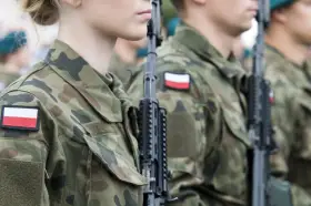 Żołnierze w mundurach z polskimi flagami, gotowi do marszu. Słychać przyśpiewki wojskowe.