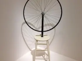 Roue de vélo fixée sur un tabouret, une œuvre emblématique de Marcel Duchamp, projetant une ombre fascinante.