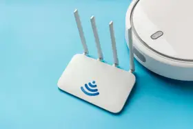 Un router Wi-Fi bianco con logo blu e un robot aspirapolvere bianco su sfondo azzurro. Cos'è un router? È il cuore della tua connessione internet.