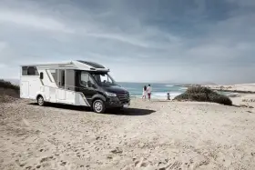 Eura Mobil husbil parkerad på en sandstrand vid havet. Ett par står och tittar ut över vågorna.