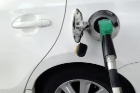 Tankowanie białego samochodu z użyciem bezkorkowego systemu wlewu paliwa. Zielona dysza dystrybutora w otworze wlewu.