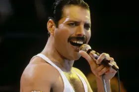 Freddie Mercury śpiewa do mikrofonu, w białej podkoszulce. Wiele osób wspomina go, kiedy zmarł Freddie Mercury.
