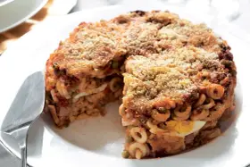 Un invitante anelletti al forno, con strati di pasta, sugo, piselli e uova sode, ricoperto da pangrattato dorato.