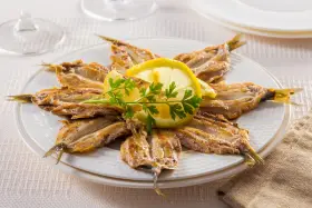 Piatto di alici alla scapece disposte a raggiera, guarnite con fette di limone e prezzemolo.