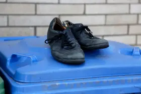 Stare, czarne buty leżą na niebieskim koszu na śmieci. Czas zastanowić się, gdzie wyrzucić stare buty, by dać im drugie życie.
