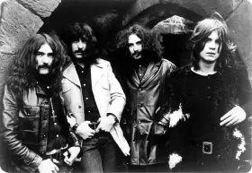 Czterech członków zespołu Black Sabbath, ikony heavy metalu, pozuje do zdjęcia. Ich mroczny styl zapowiadał przełomowe black sabbath albumy.