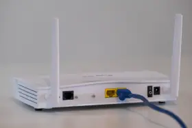 Biały modem z dwiema antenkami, podłączony niebieskim kablem Ethernet. To urządzenie, które pozwala na połączenie z internetem.