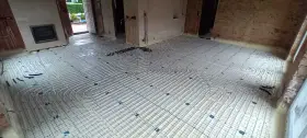 Installation d'un plancher chauffant en cours de renovation. Les tuyaux blancs sont posés sur des panneaux isolants, prêts à être recouverts.