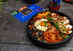 Pyszny Bibimbap przepis: ryż, kurczak, jajko sadzone, grzyby, marchewka i kimchi. Obok opakowanie pasty kimchi.