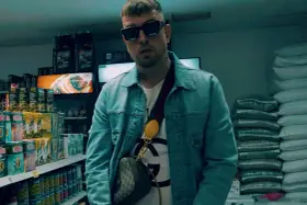 Sentino Malik w dżinsowej kurtce i okularach stoi w sklepie, otoczony towarem.