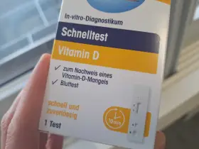 Hand hält eine Verpackung für einen Vitamin-D-Schnelltest mit einem Bluttest-Streifen.