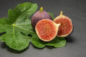 Dos higos morados, uno entero y otro partido por la mitad, reposan sobre hojas verdes y húmedas. ¡Qué delicia, los higos engordan!